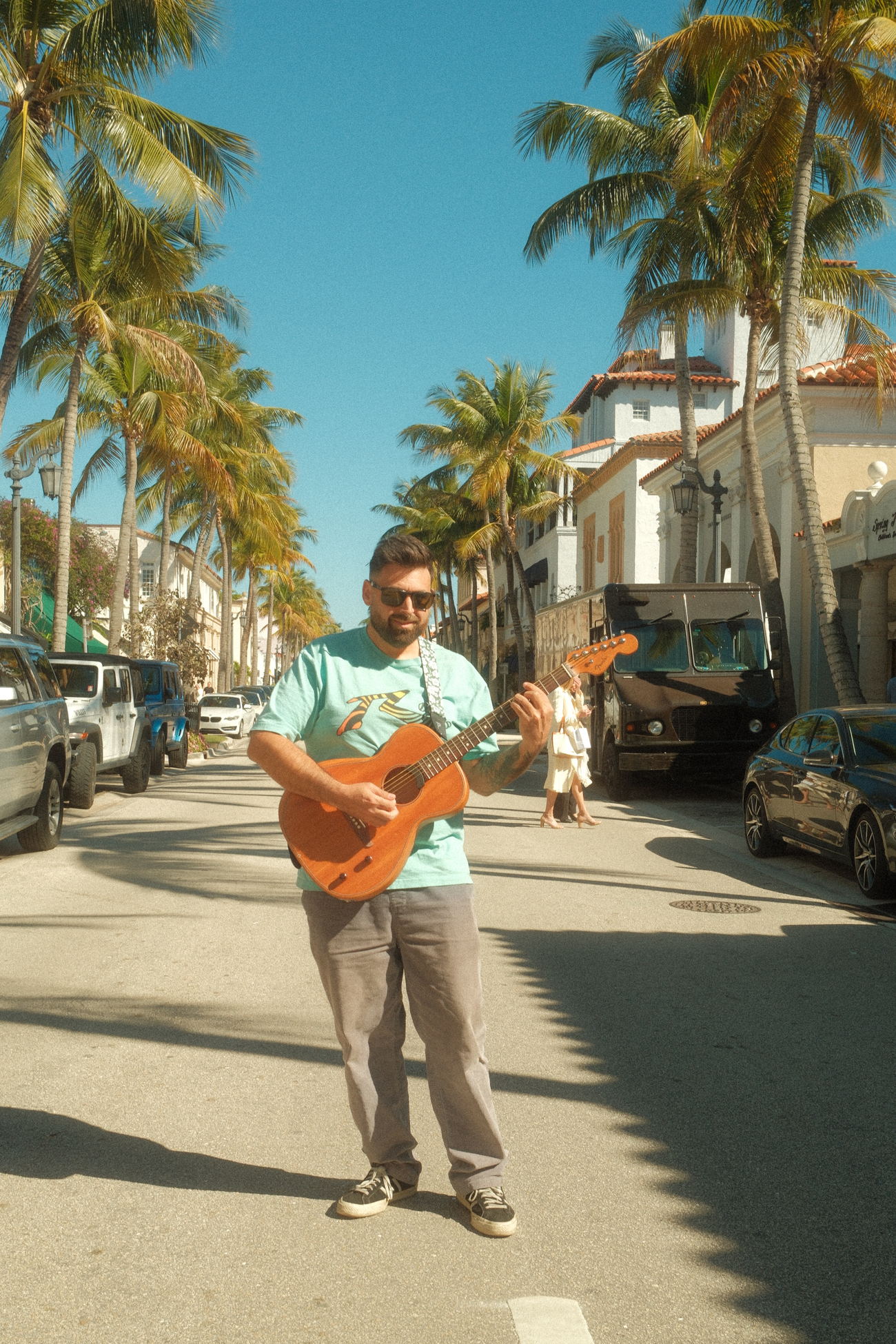 Kairo Reef standing in a palm-lined street with an acoustic guitar